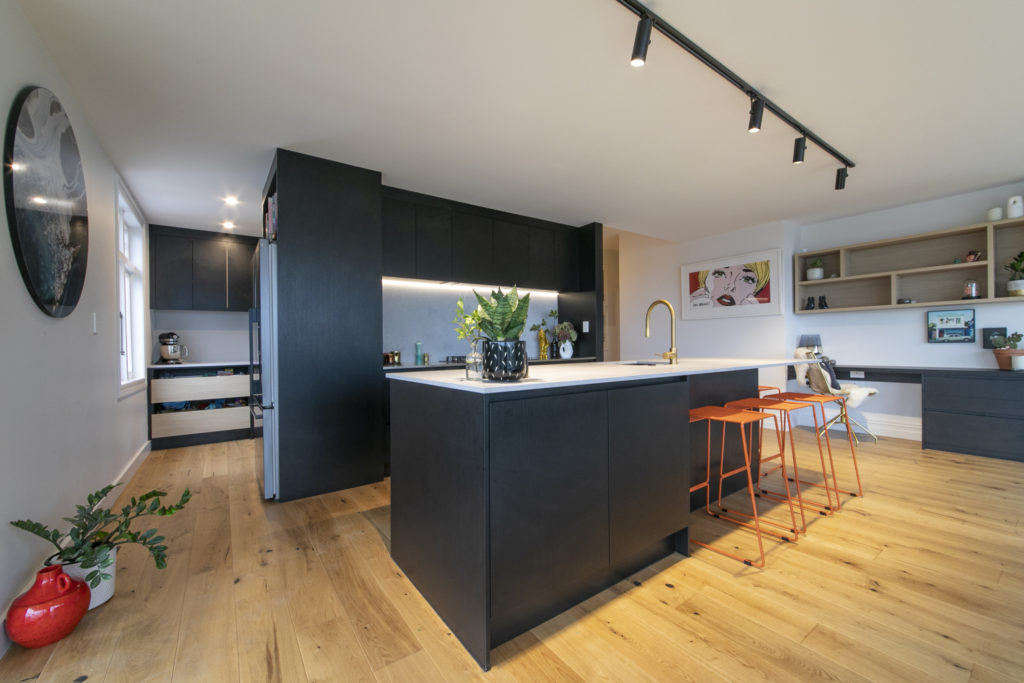 Black kitchen with orange bar stools and gold tap